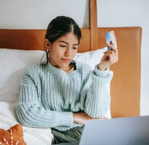 girl holding a credit card sitting in bed with a laptop
